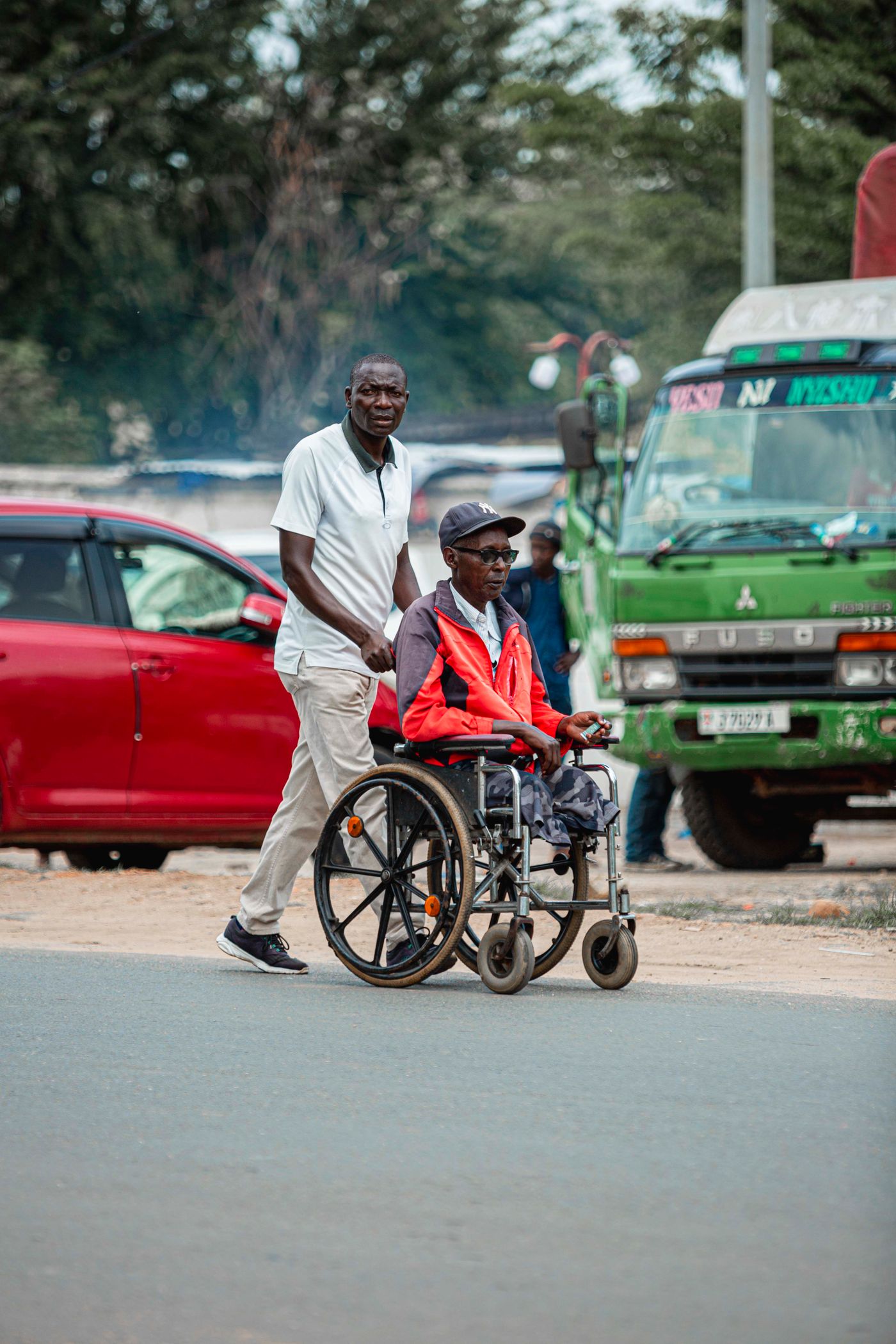 A support worker walking with a man in a wheelchair along a city street