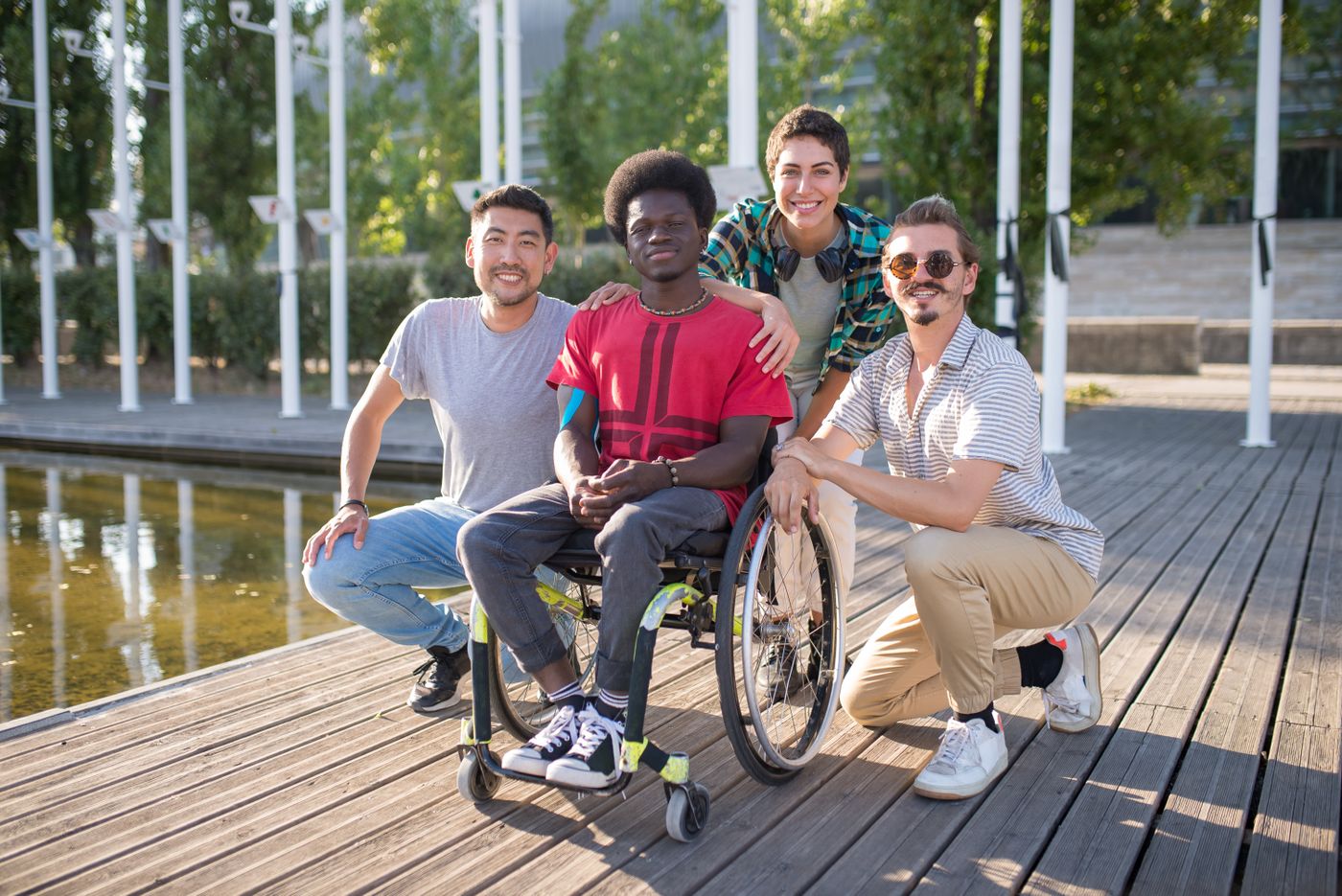 A group of friends laughing together outdoors, one using a wheelchair