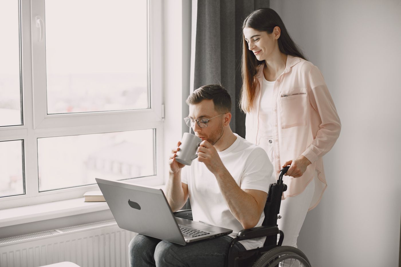 A man in a wheelchair using a laptop with a friend beside him