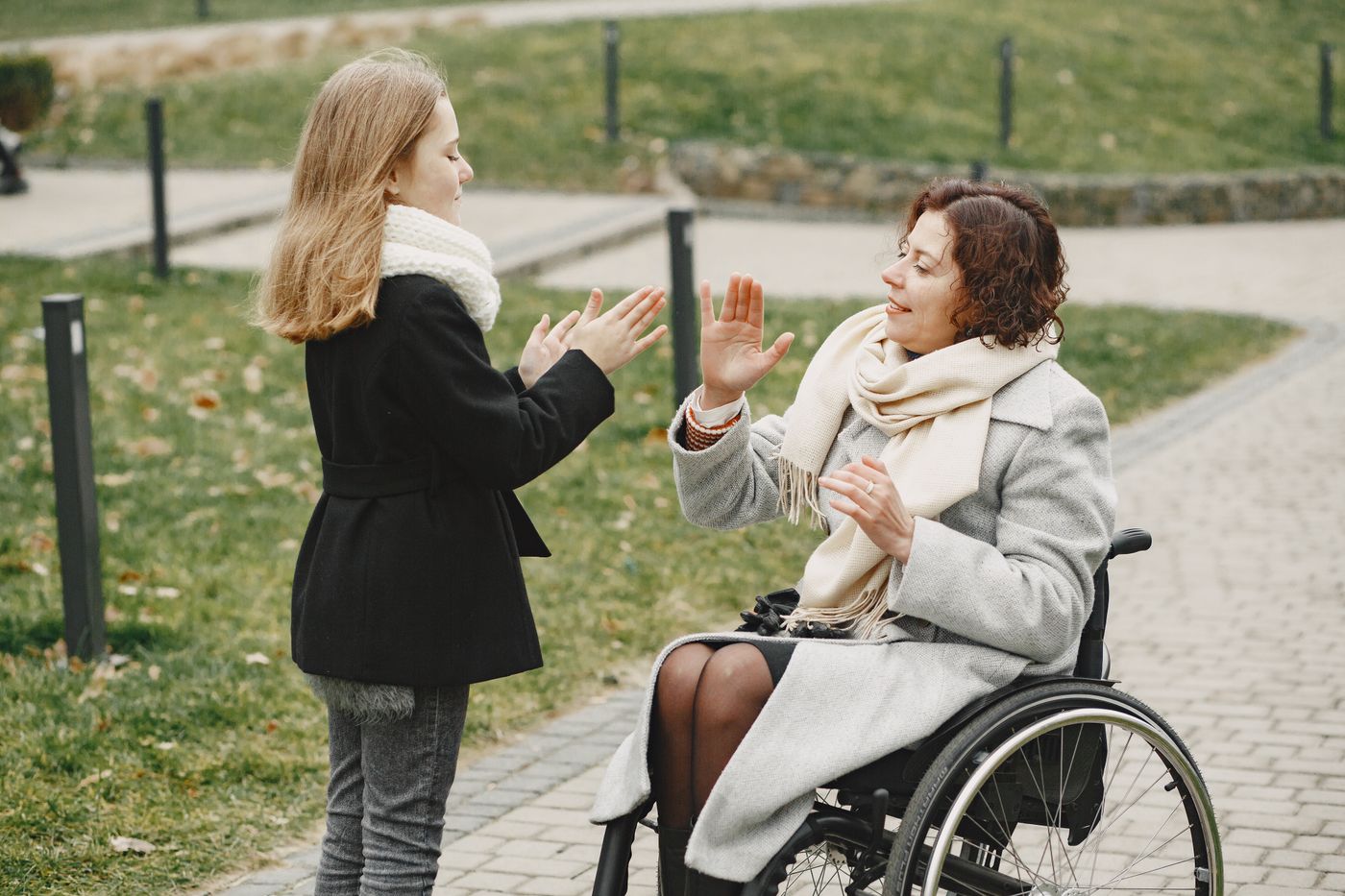 Two women talking and laughing in a park, one using a wheelchair